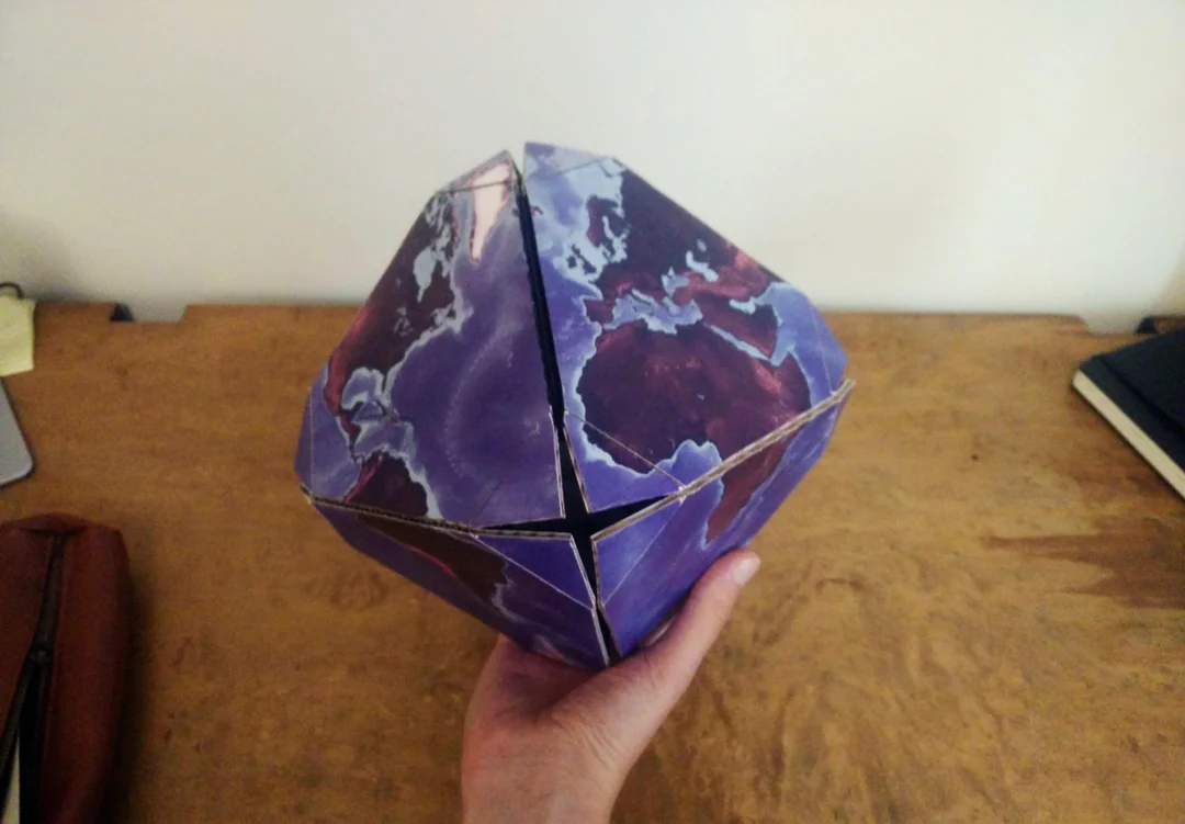 A truncated octahedron made out of cardboard with oceans and continents printed onto it
